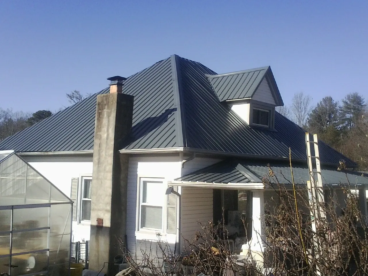 Dark blue standing seam metal roof on a white farmhouse with dormer — Slate & Tile Roof Repair by Roofing Brothers in Lubbock