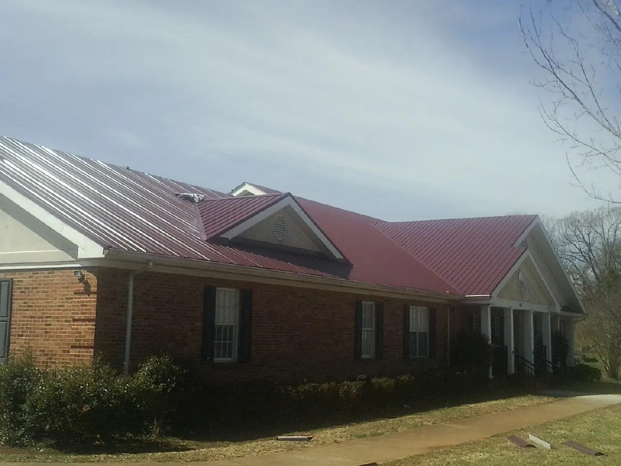 Red metal roof with gabled entries on a long brick building, from a Hail Damage Roof Repair job in Lubbock