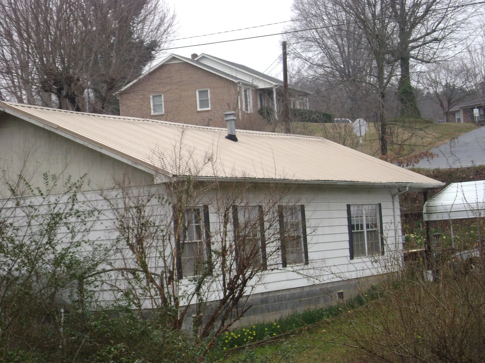 Tan metal roof on a white sided house set into a hillside — Commercial Roofing by Roofing Brothers in Lubbock